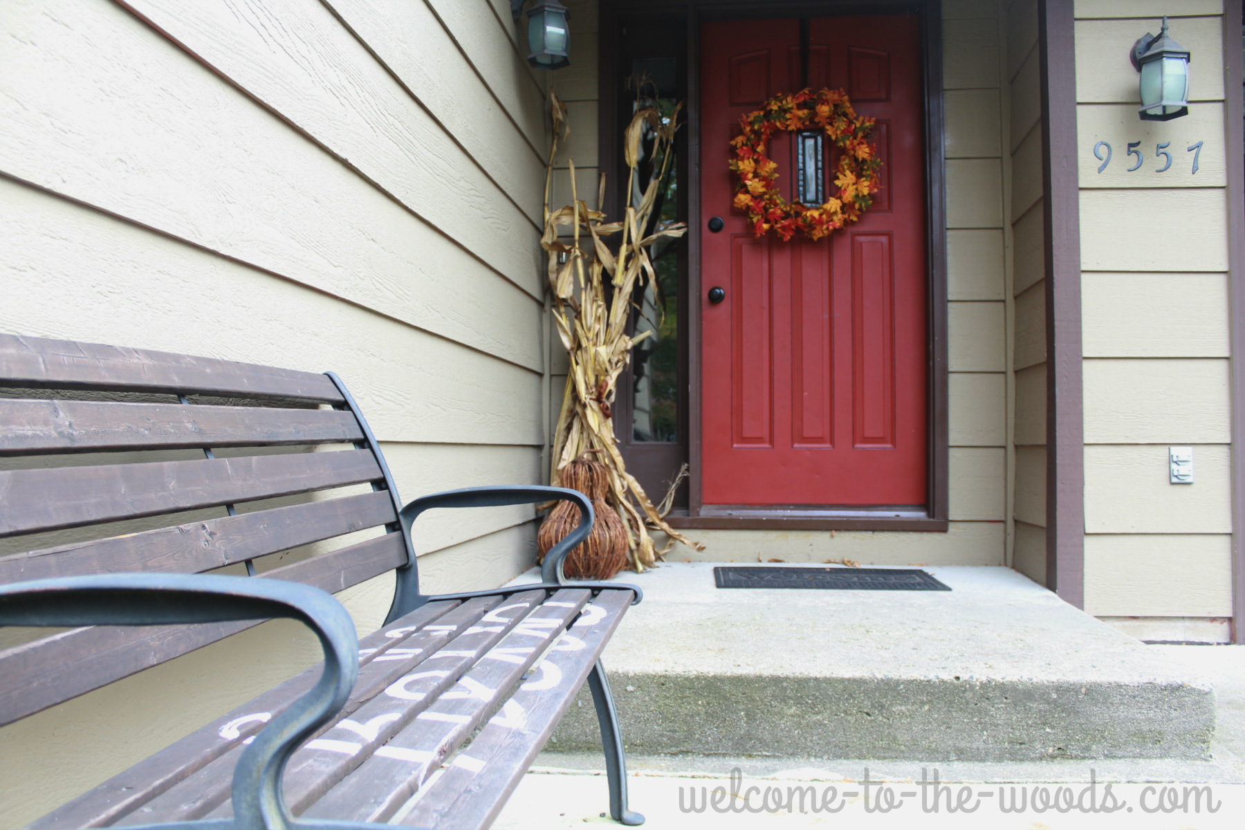 Front entrance fall decor, wood bench with "Hello" sign, leaf wreath, corn stalks, and gourds.