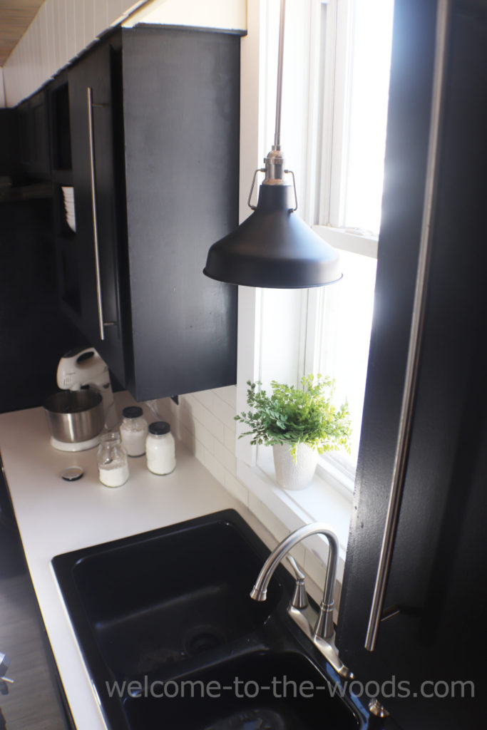Pendant light hanging over the sink in front of window in kitchen with black cabinets white counters
